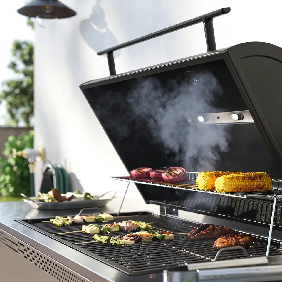 Black outdoor bbq grill with lid open, grilling steaks, vegetables, and corn. Smoke rises, tongs and plates nearby.