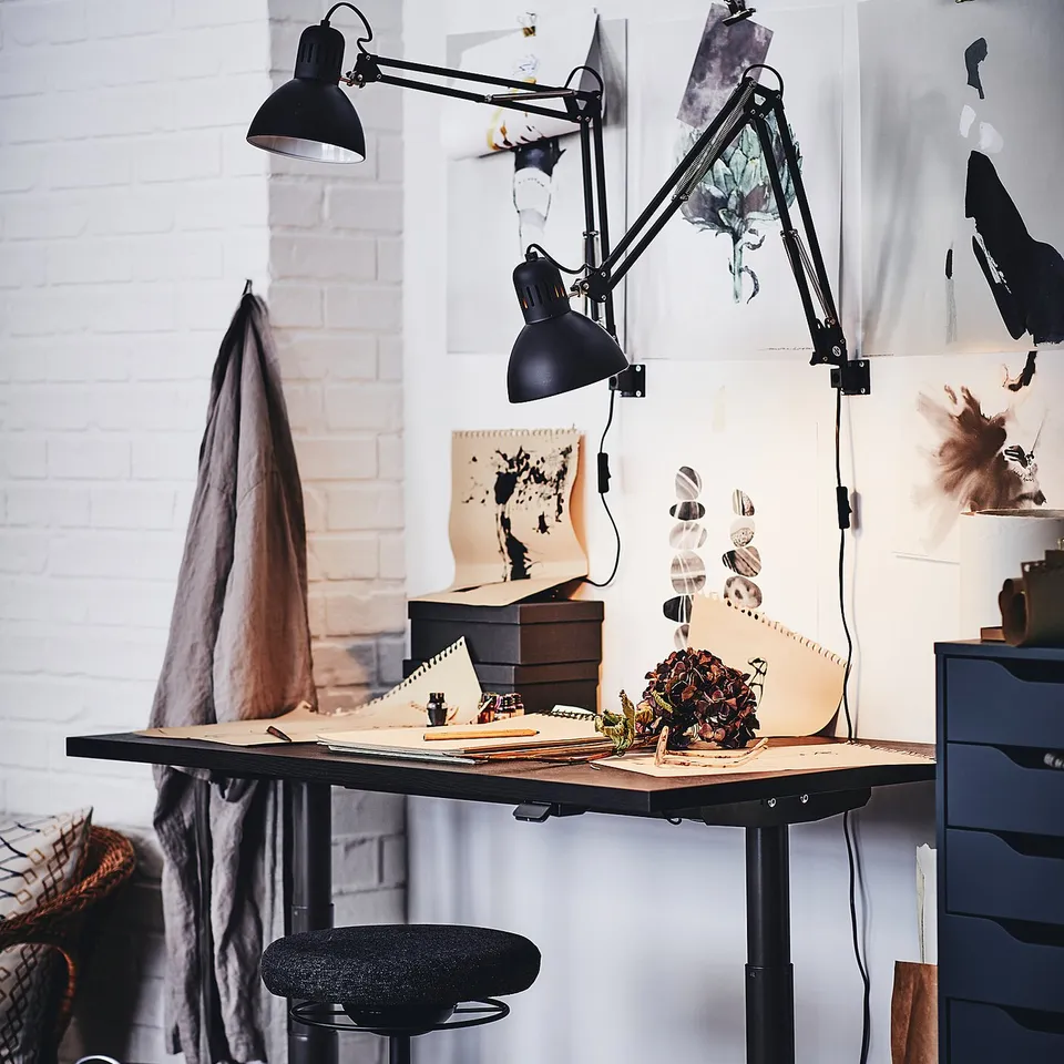 Artistic workspace with TERTIAL black lamps, wooden desk, modern chair, and wall posters. Bright and inspiring setup.
