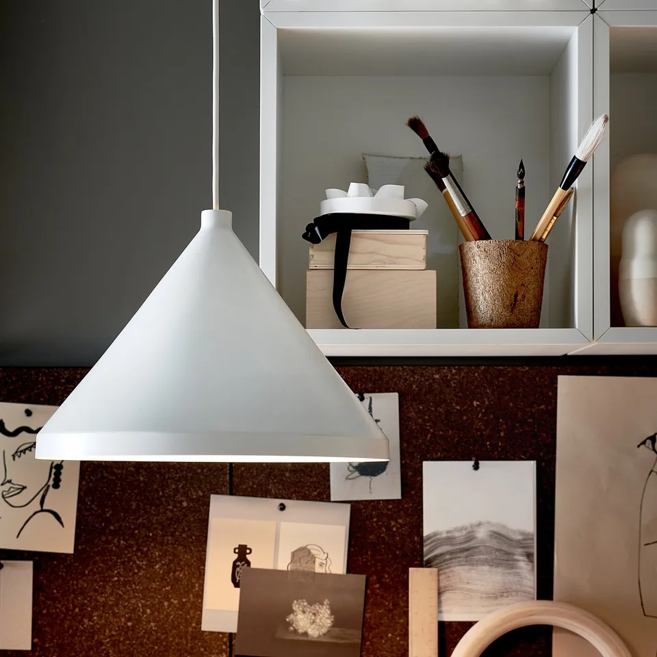 Modern grey pendant lamp hangs near organised shelves with art supplies and drawings.