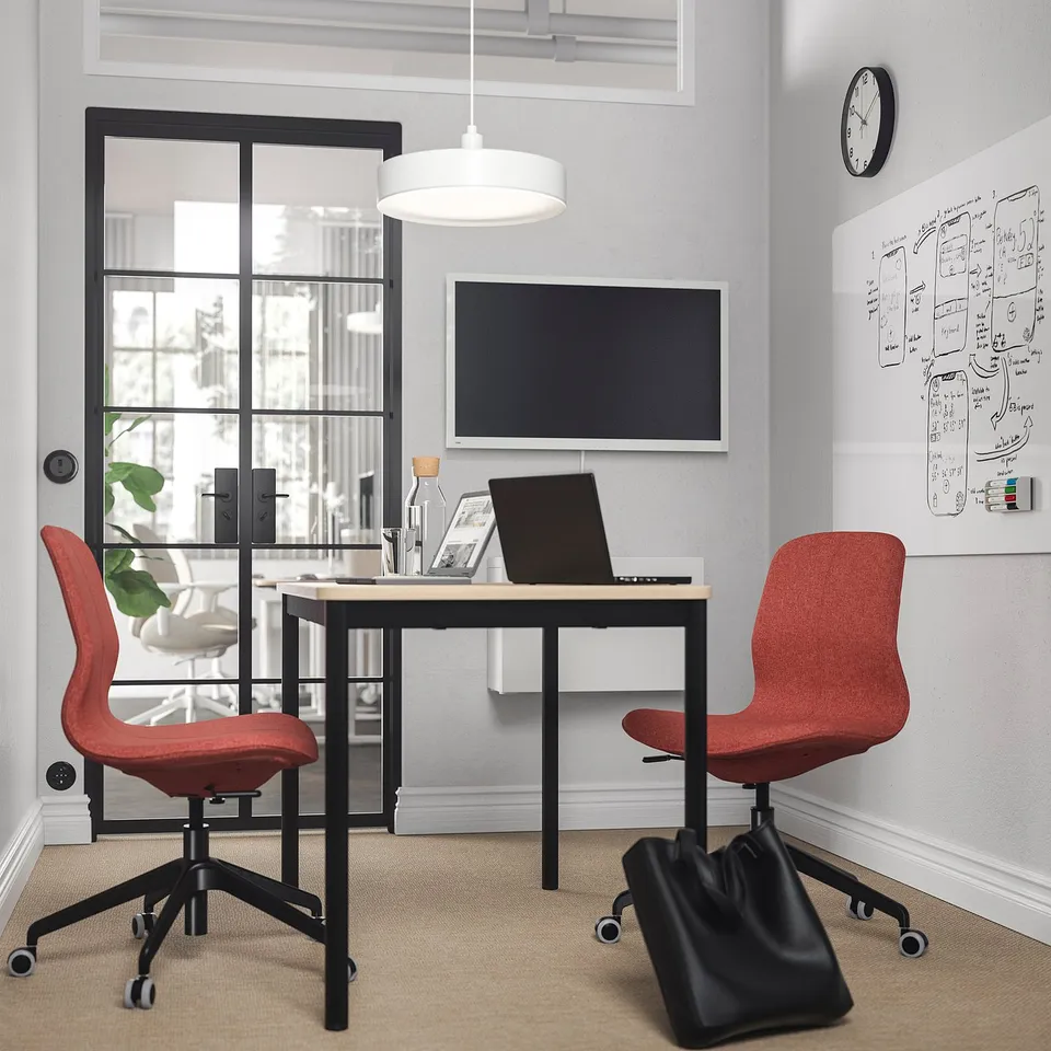 Minimalist office with two red LÅNGFJÄLL chairs, black desk, and large window. Chairs match white pendant lamp and wall clock above.