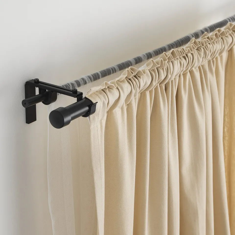 Black curtain rod system with adjustable, pleated beige curtains on wall, showcasing flexible design for various looks.