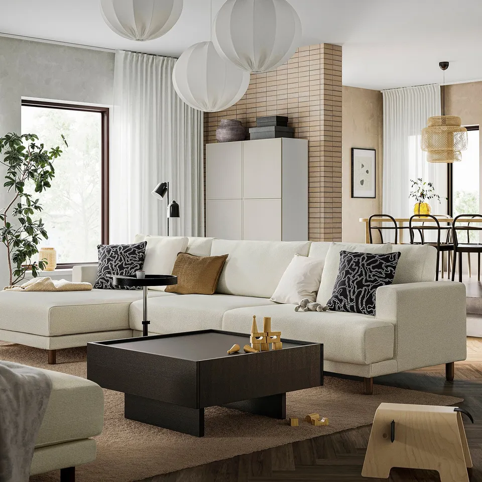 Modern living room with cream UPPÅKRA sectional sofa, black pillows, dark coffee table, white cabinet, large windows, and pendant lights.