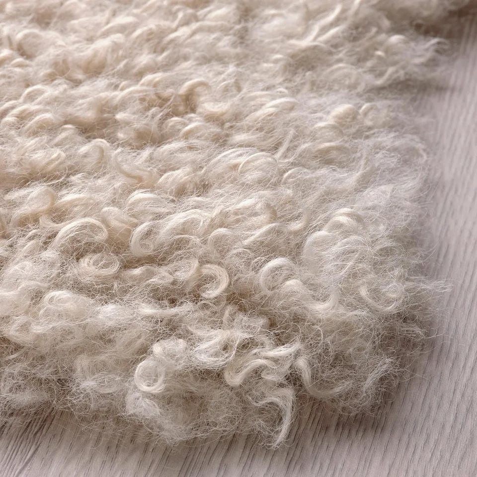 Soft, plush rug texture close-up, natural beige colour, curly fibres on wooden floor.