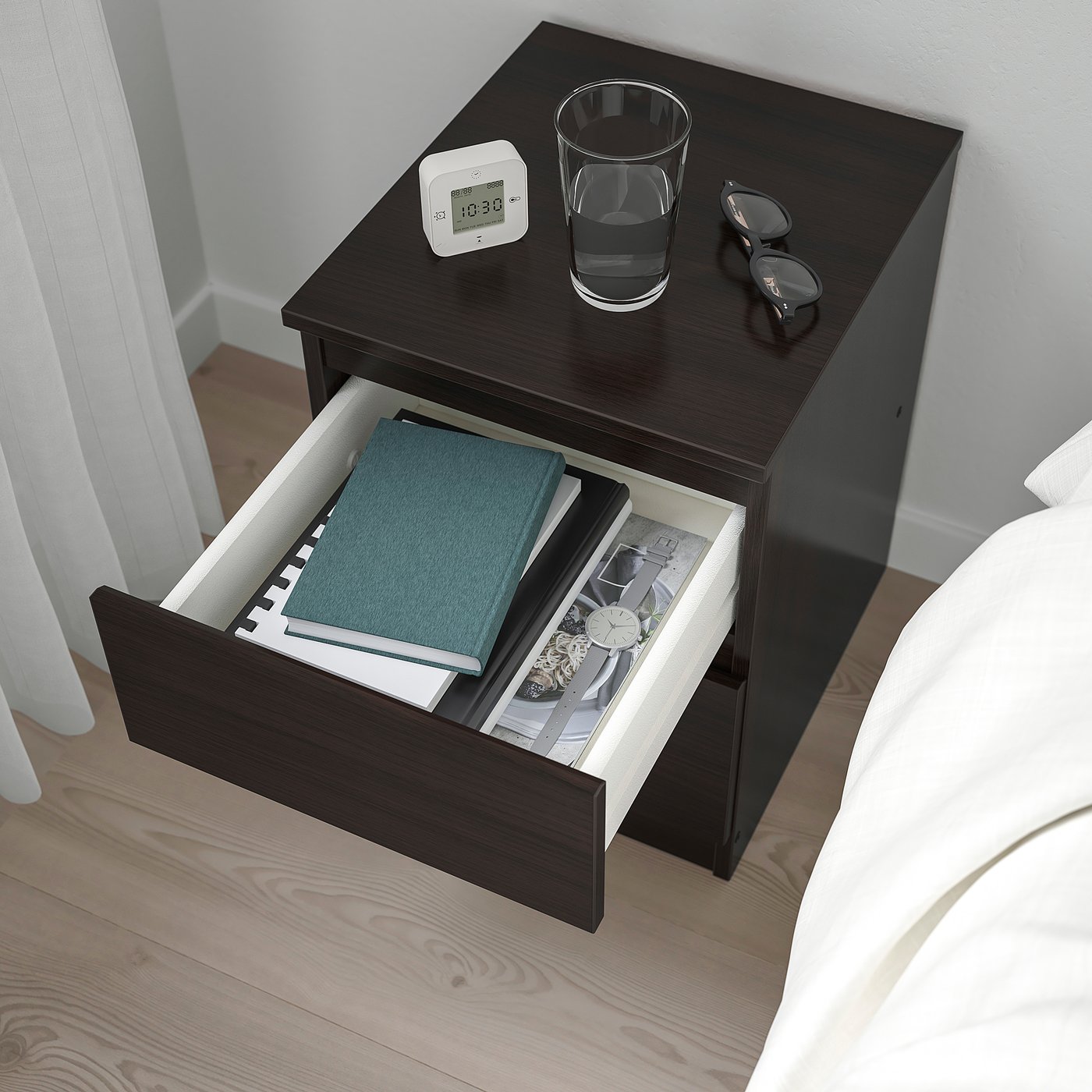 Wooden bedside table with open drawer showing books and a clock on top.