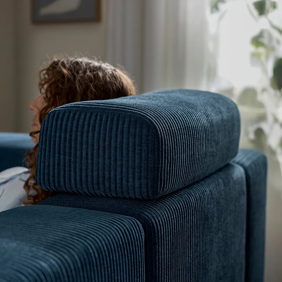 Person resting on blue JÄTTEBO sofa with headrest.