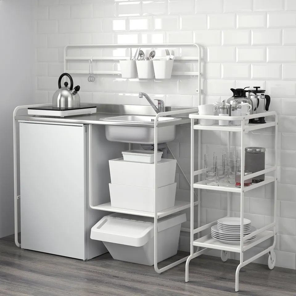 Compact kitchen setup, featuring sink, storage bins, and utensils on a shelf, with a kettle on the counter.