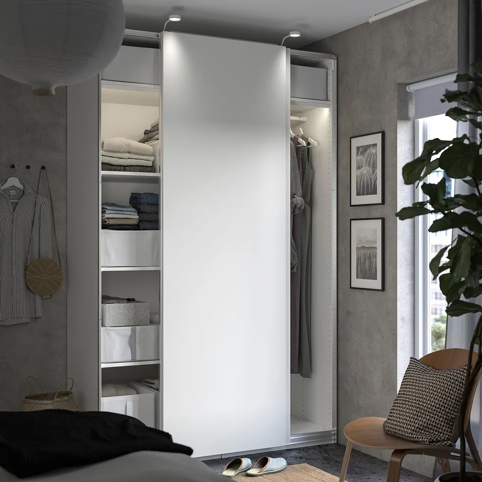 Modern bedroom with white PAX wardrobe, framed pictures, wooden chair, and plants.