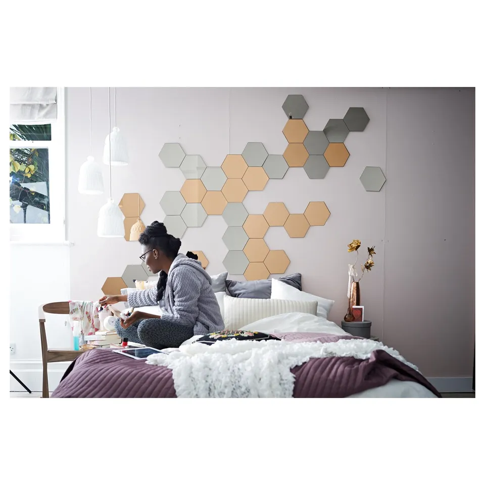 Bedroom with person reading on bed, hexagon mirrors on wall.