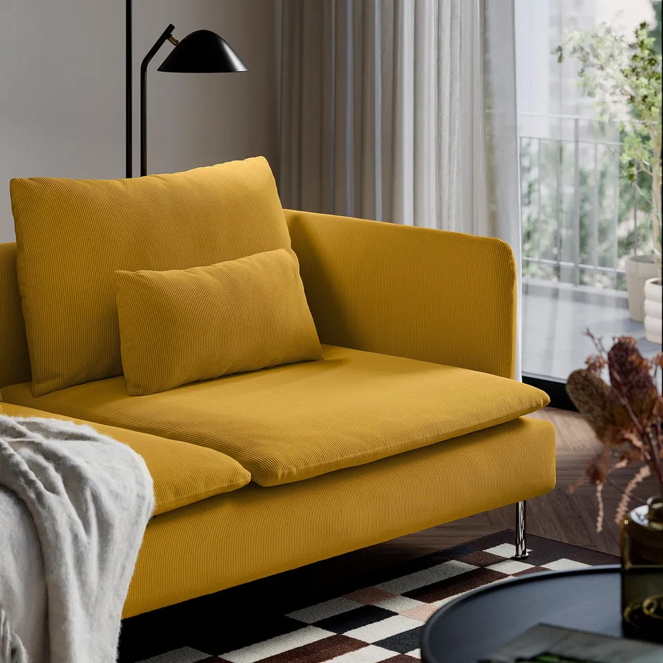 Yellow sofa with 2 pillows, blanket, tall lamp, high legs, by window.