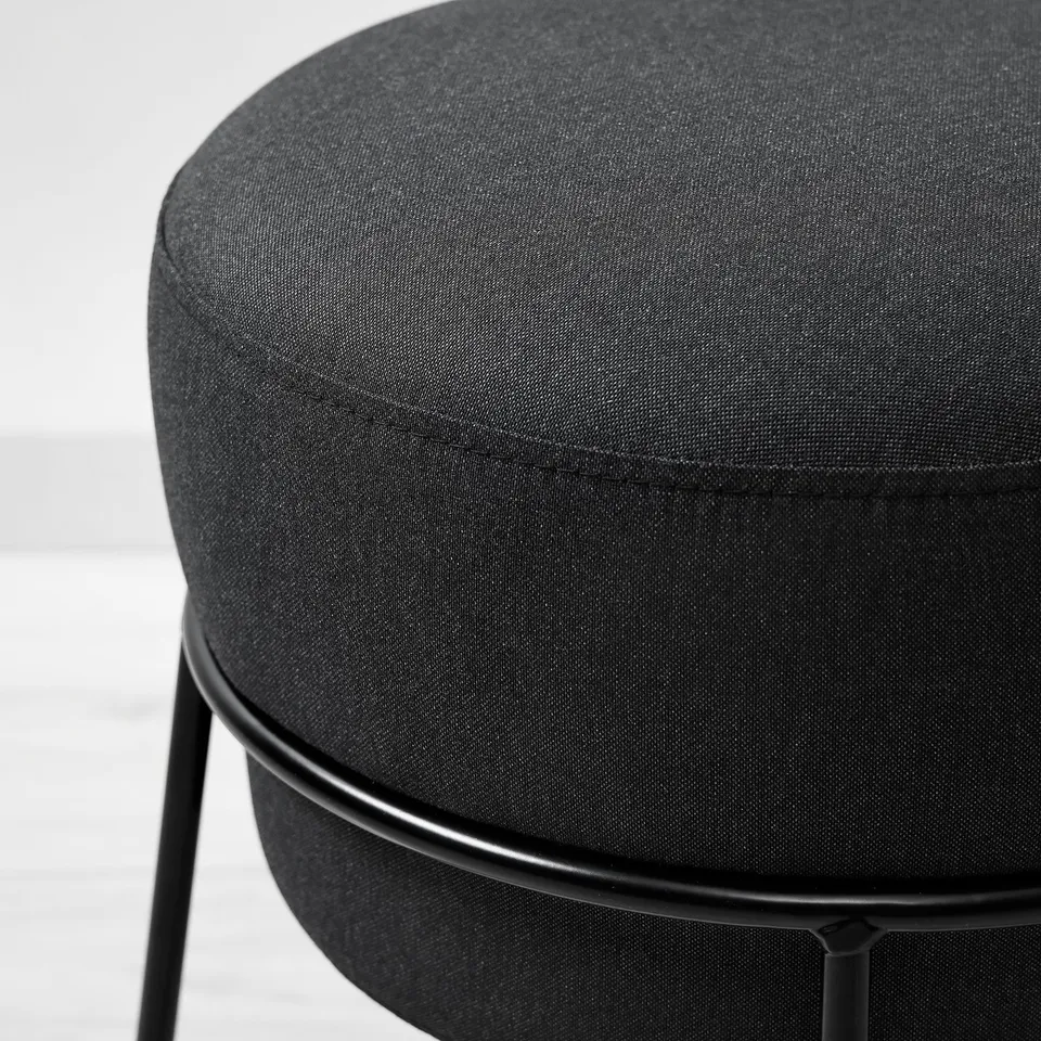 Modern round footstool with sleek black metal frame and plush, dark grey fabric cover, offering comfort and contemporary style.