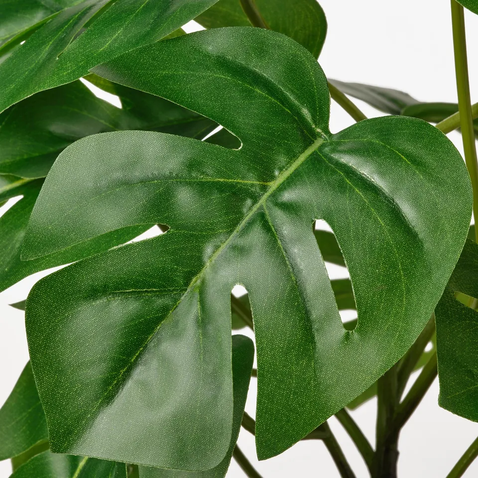 Close-up of lifelike fake plant with large, glossy green leaves, resembling a real plant.