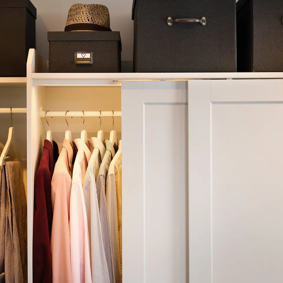 Well-organized closet with hanging dresses on left, storage boxes on top shelf, featuring white colours and metal accents.