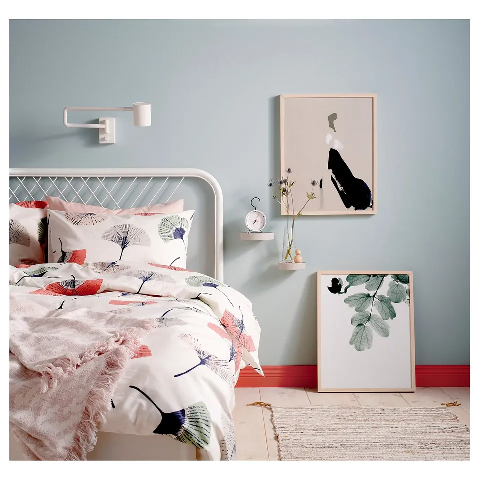 Modern bedroom with white metal bed, floral bedding, blue walls, abstract art, and wall-mounted light.
