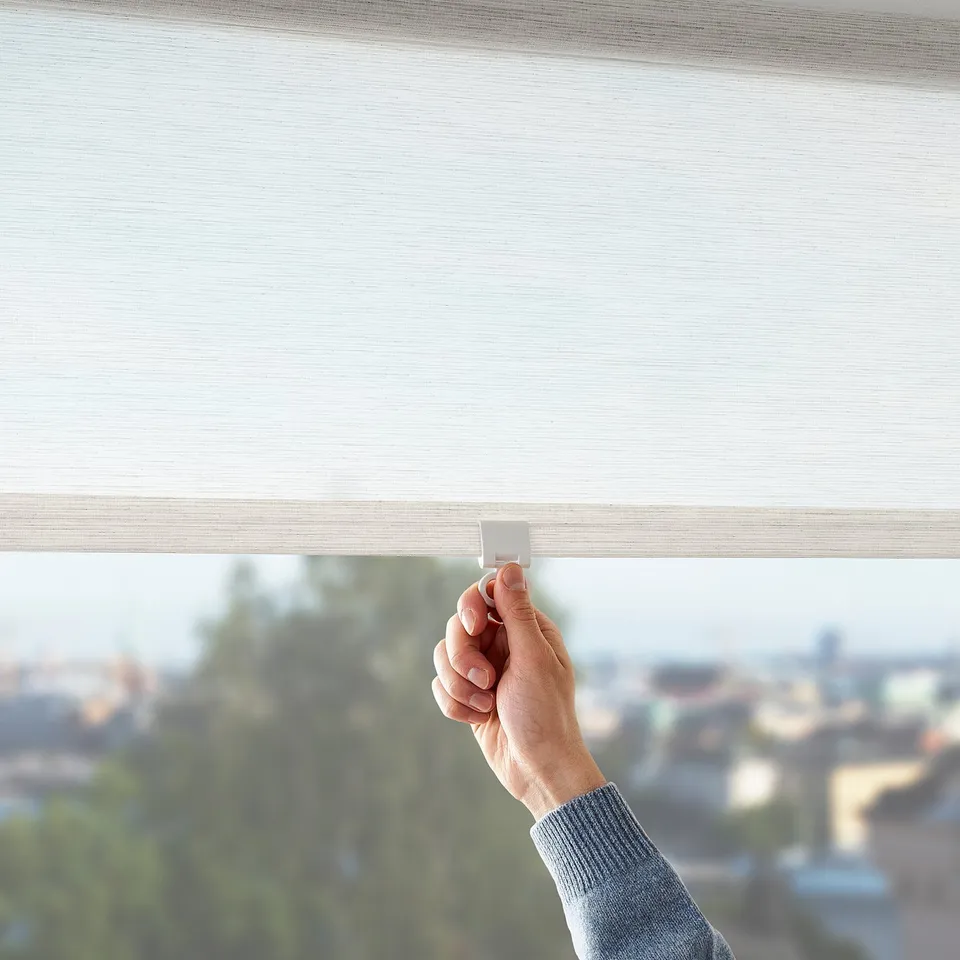 Person holding light-filtering roller blind, adjusting it to control room light and privacy.