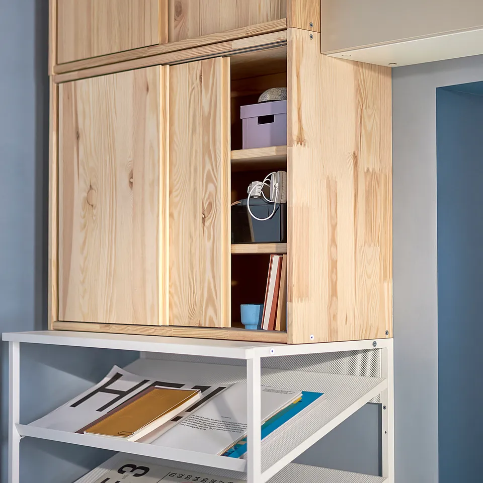 IVARs pine storage unit with sliding door, holding various items.