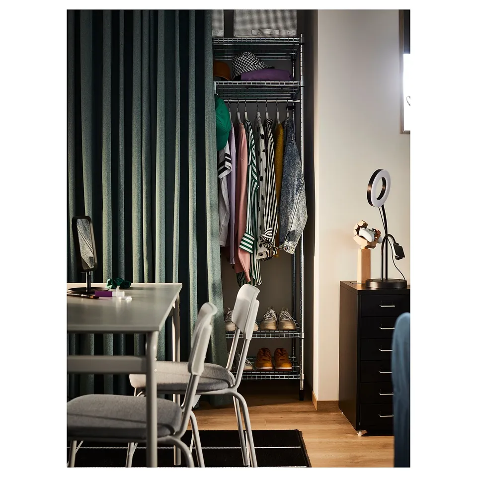 Modern bedroom with black shelving, clothes, dark curtain, grey chair, desk, unique lamp.