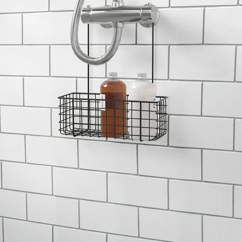 Metal wire basket hangs in shower, holding two bottles of shower gel or shampoo against tiled wall. Part of the BLECKSJÖN series.