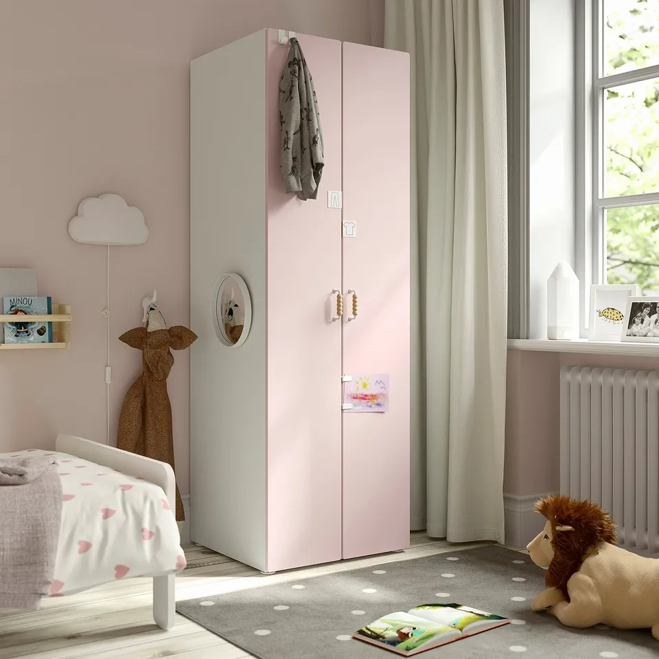 Pink SMÅSTAD wardrobe with mirror, clothes rail, near bed with heart bedding, window, lion toy, dot rug.