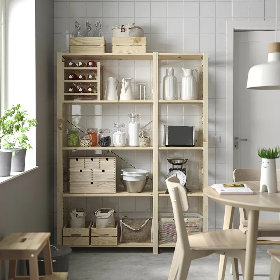Wooden IVAR shelf with pitchers, jars, and boxes by window with plants and table.