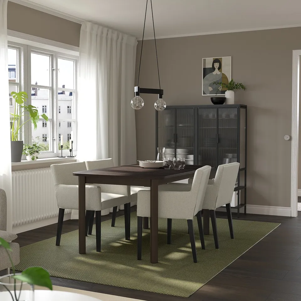Modern dining room with extendable table, grey chairs, black lights, sideboard, large window, and green rug.