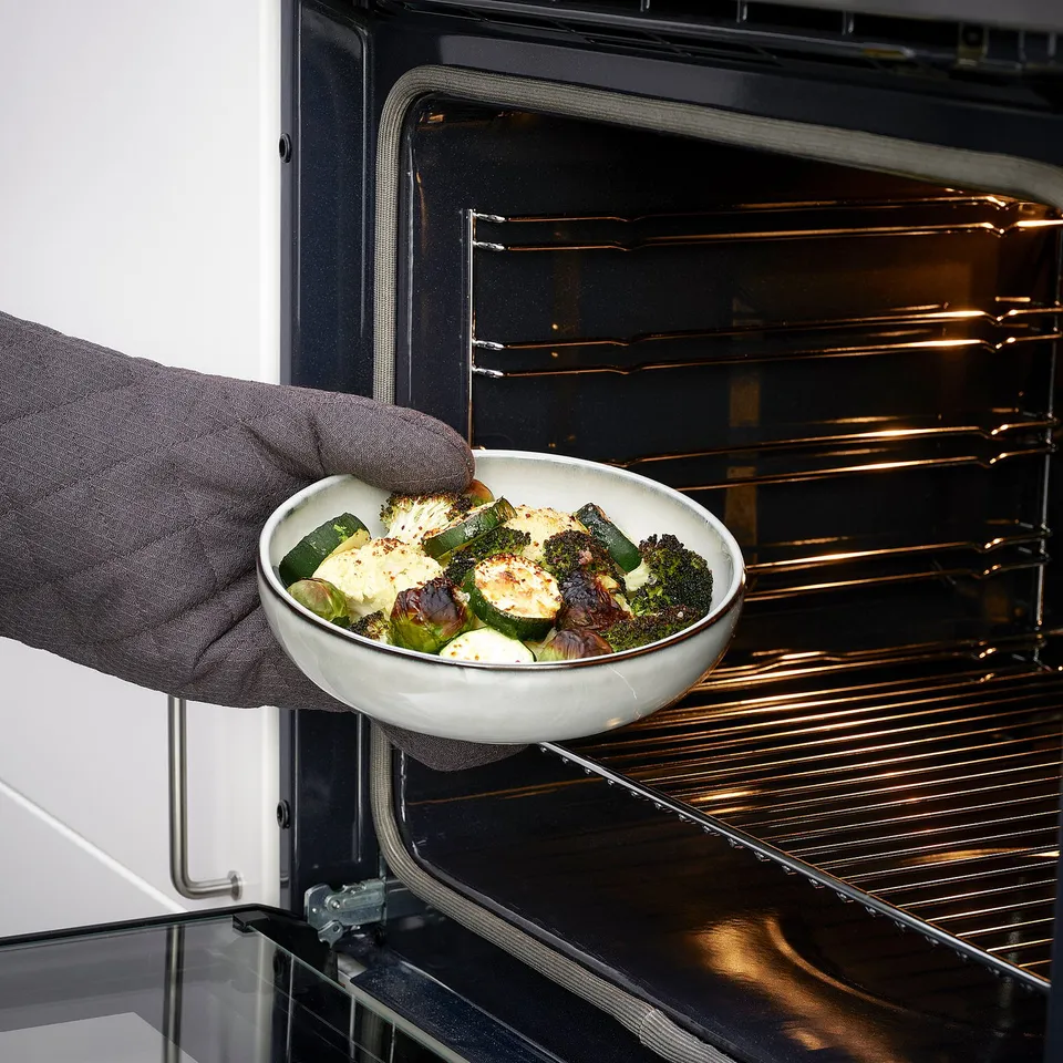 Person placing baked dish into oven. Product: GLADELIG oven dish.