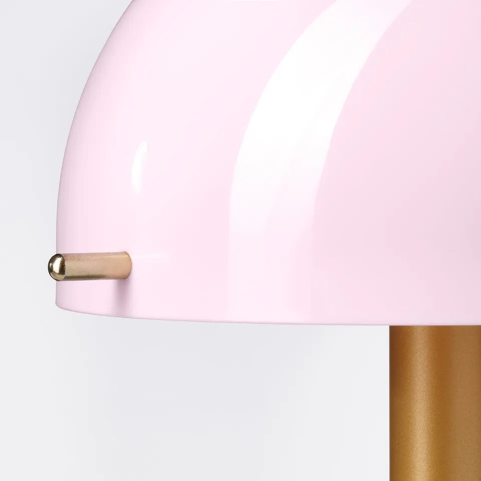 Displays a close-up of a modern pastel pink lamp with a gold accent and white base.