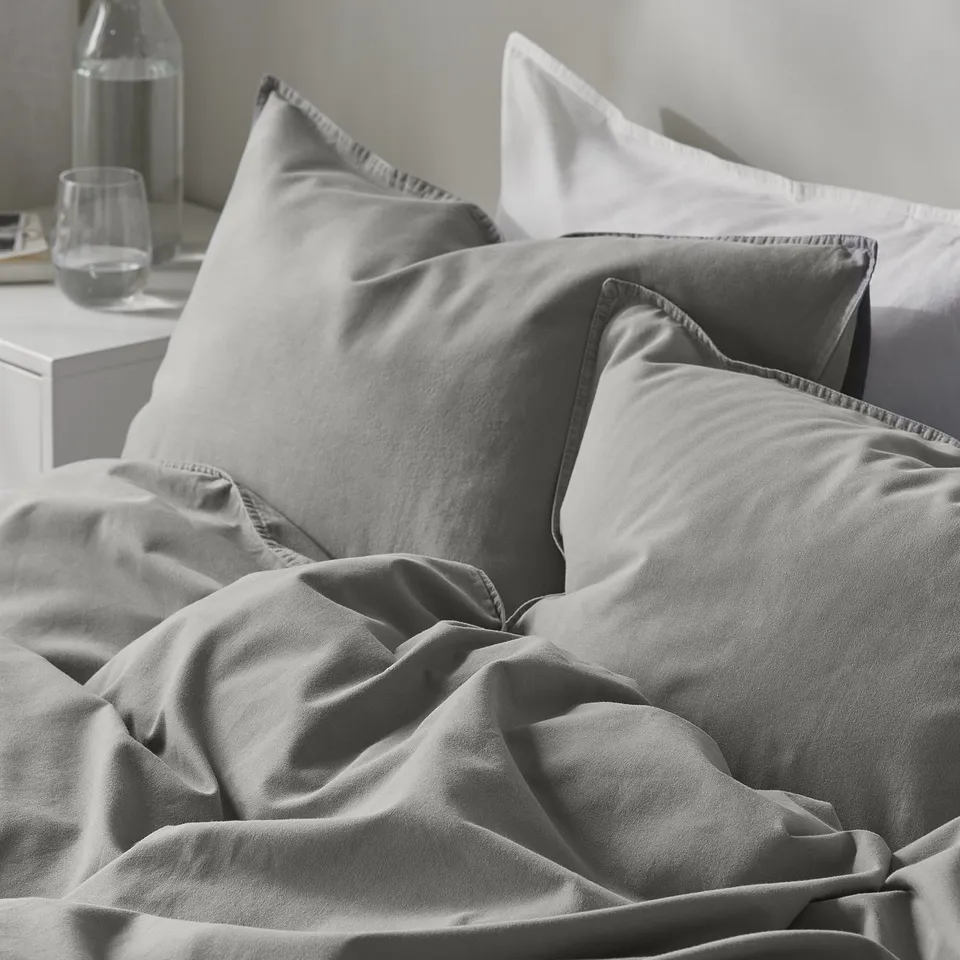 Bed with soft, grey duvet and pillows. Comfortable, high-quality cotton bedding.