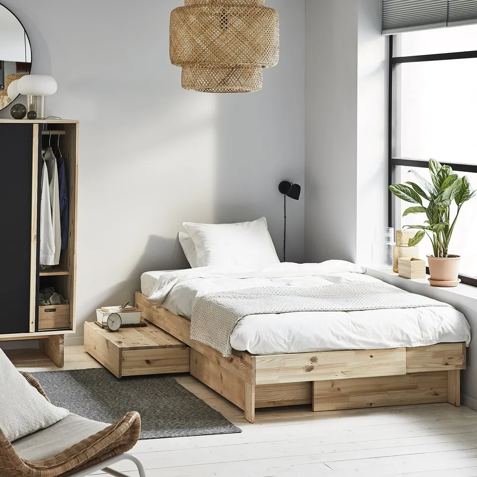 Modern bedroom with GLAMBERGET extendable pine bed, white linens, wicker pendant light, and a plant.