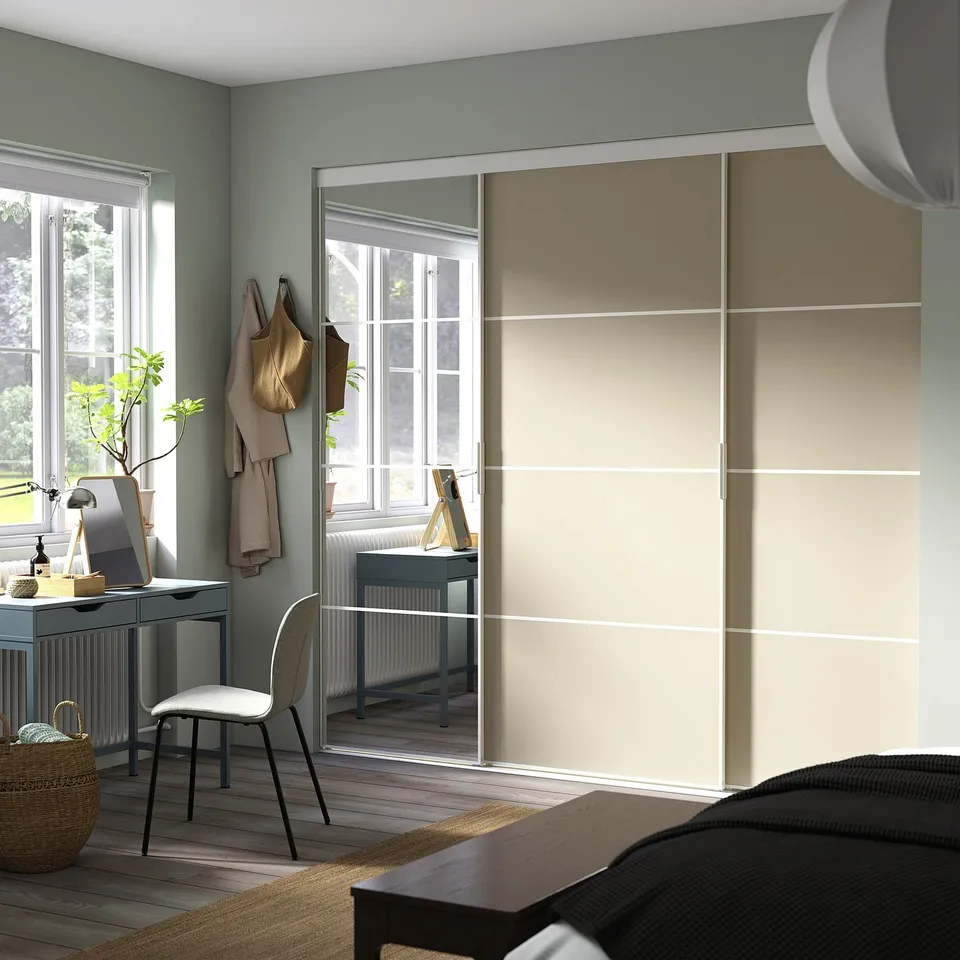 Modern bedroom with large mirrored SKYTTA wardrobe, desk under window, cosy chair, and decor.