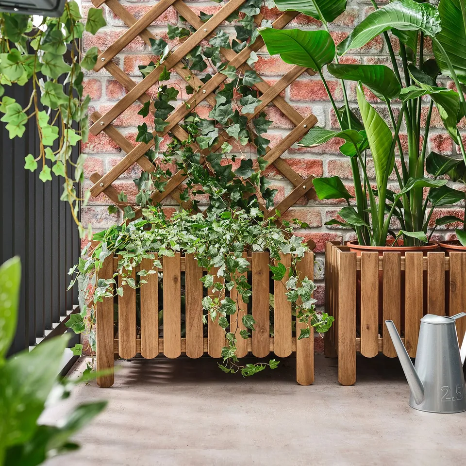 Wooden ASKHOLMEN plant stand with climbing greenery against brick wall, watering can nearby.