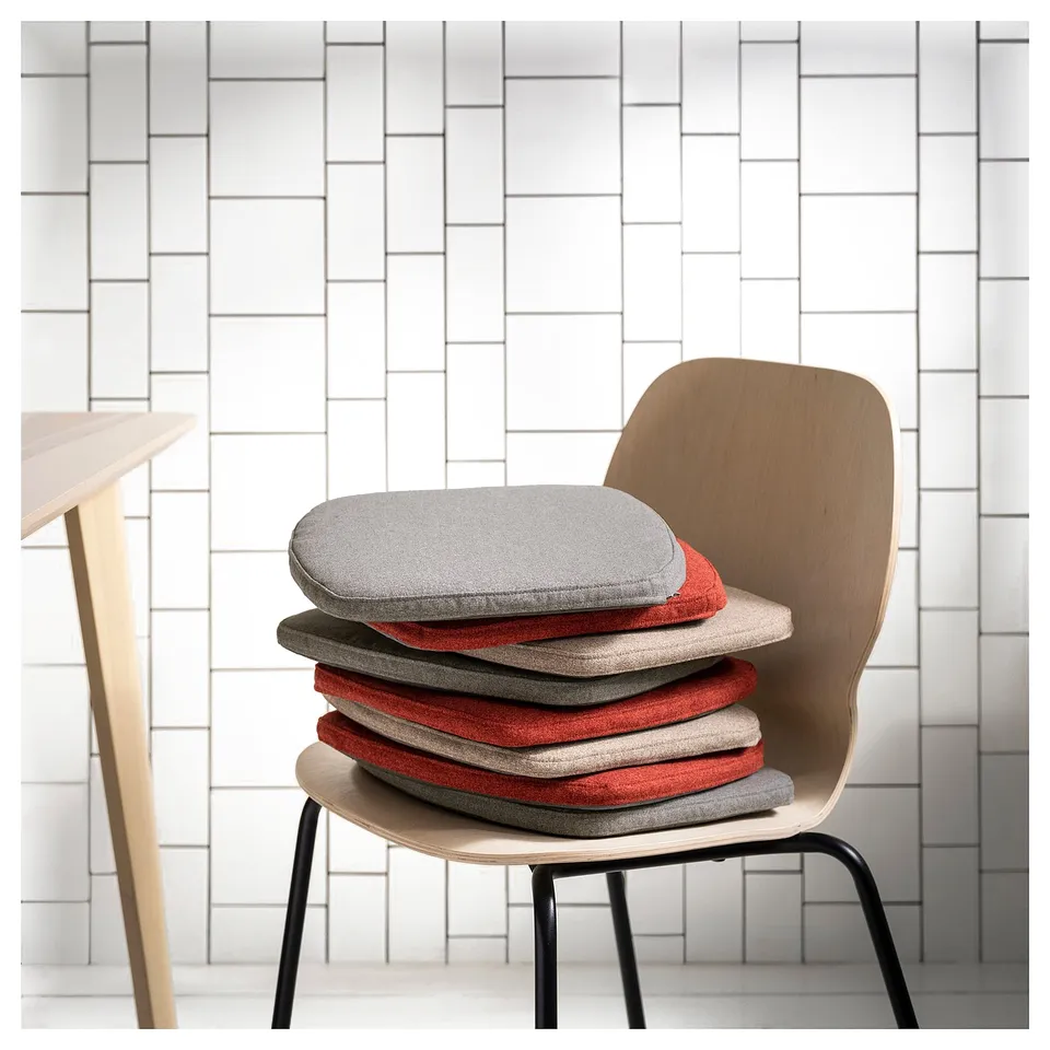 Modern chair pads in grey and red, minimalist design, recycled materials, against white wall.