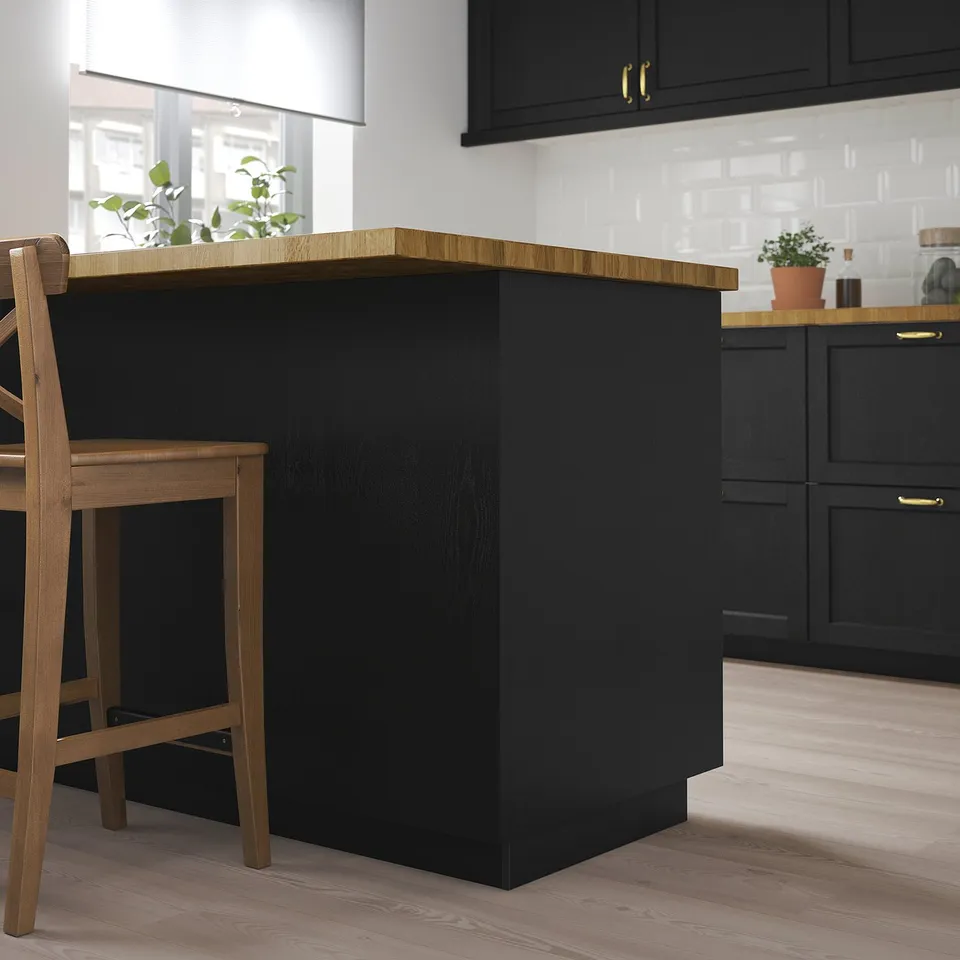 Modern black kitchen island with wooden countertop, flanked by wooden chairs. The island contrasts with white tiled backsplash and black cabinets.