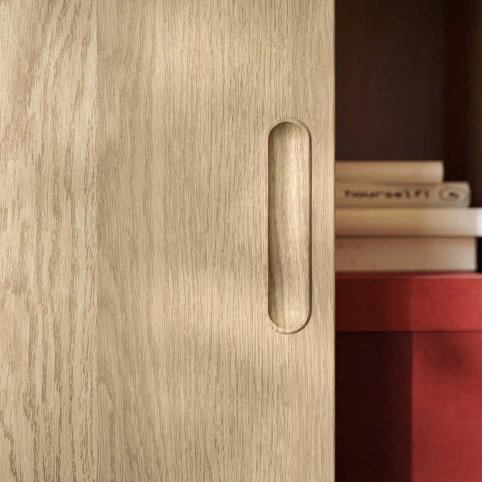 A close-up of a light wood cabinet door with a narrow, oval handle.
