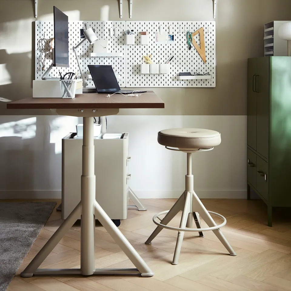 Modern home office with IDÅSEN desk and stool, light-colored desk with computer, cushioned round stool, and wall-mounted pegboard.