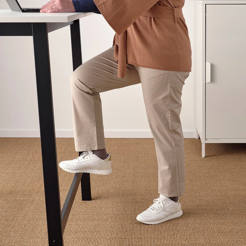 Standing desk setup with person using laptop and footrest for support.