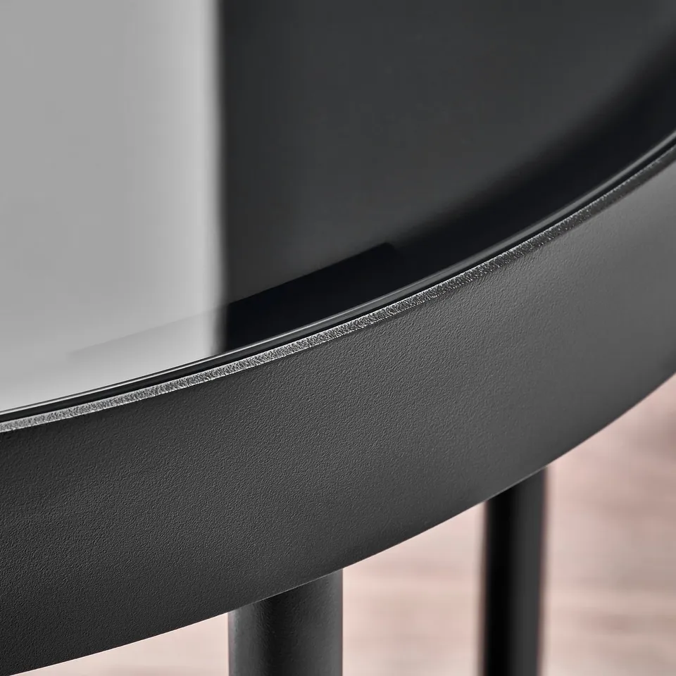Black round dining table with smooth, glossy surface and sleek metal legs, shown in close-up.
