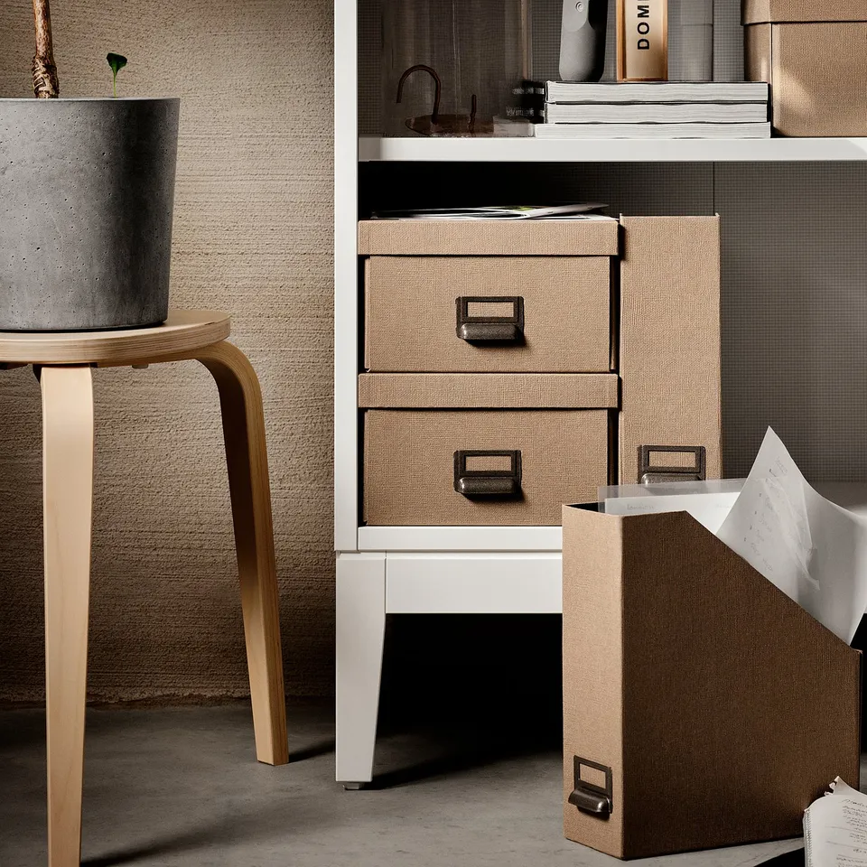 Displays a modern white IDANÄS storage unit with natural texture drawers and a concrete planter on a wooden stool.