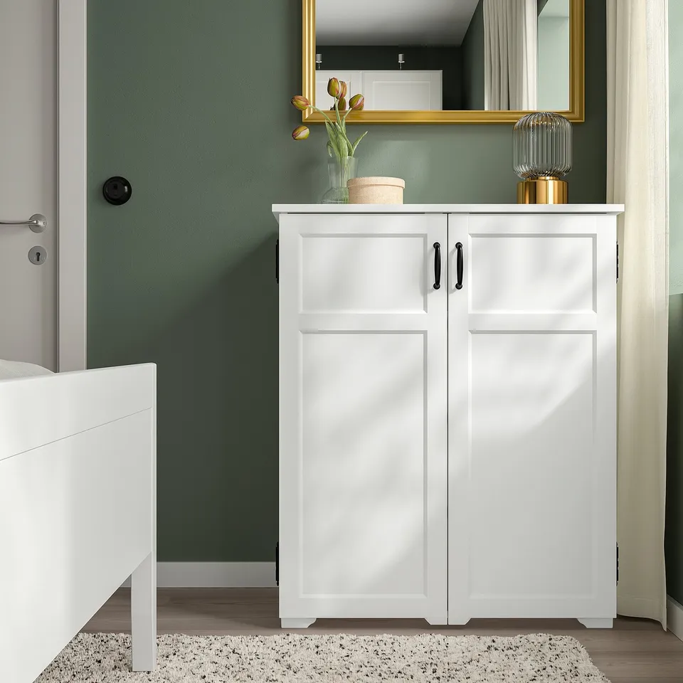White GREÅKER cabinet with 2 doors, green wall, knitted rug, bed frame, mirror, decor.