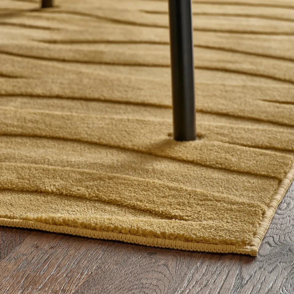 Gold-colored textured rug with a 3d wave pattern and a black pole in the centre, likely for stability.