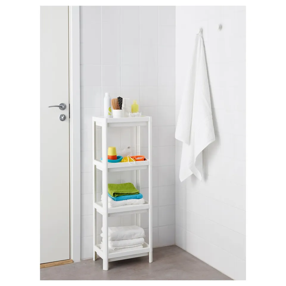 Tall white VESKEN shelf in bathroom with towels and toiletries, next to door.