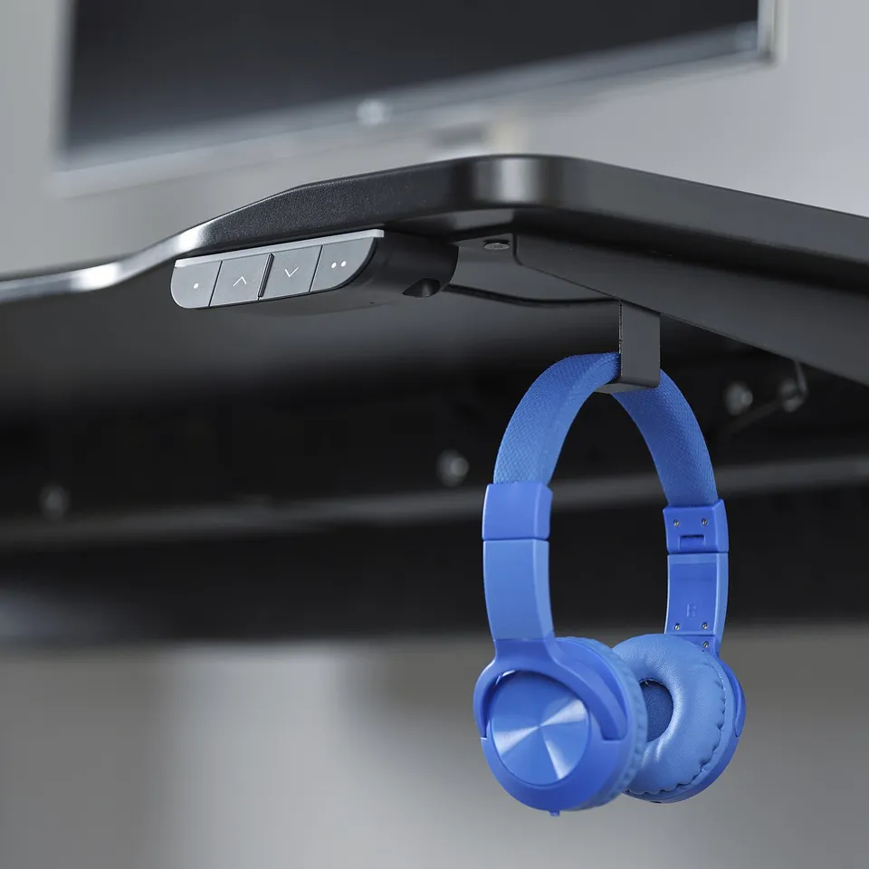 Blue headphones hang on a black gaming desk with an electric height adjuster.