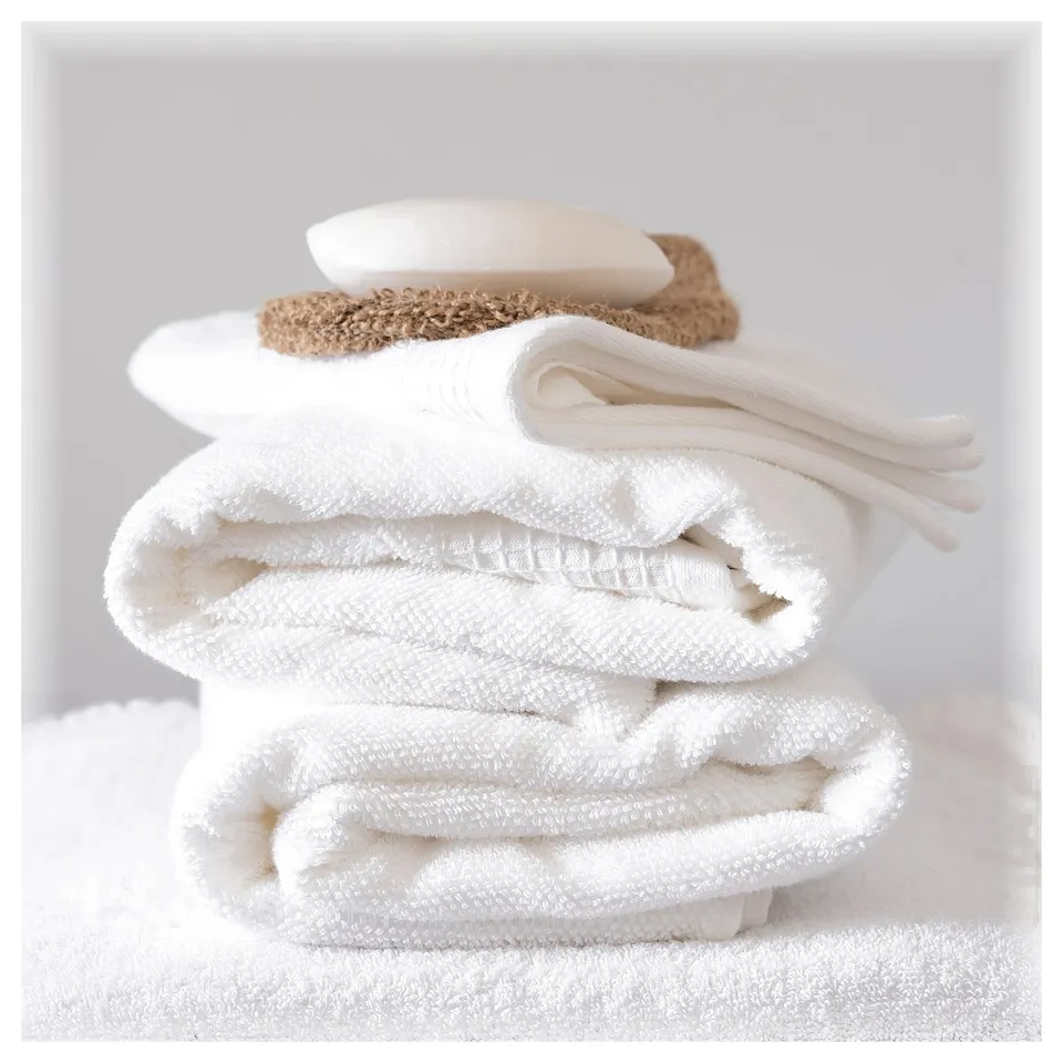 Stack of folded white towels with a beige soap on jute mat, neatly arranged. Clean, minimalist bathroom scene.