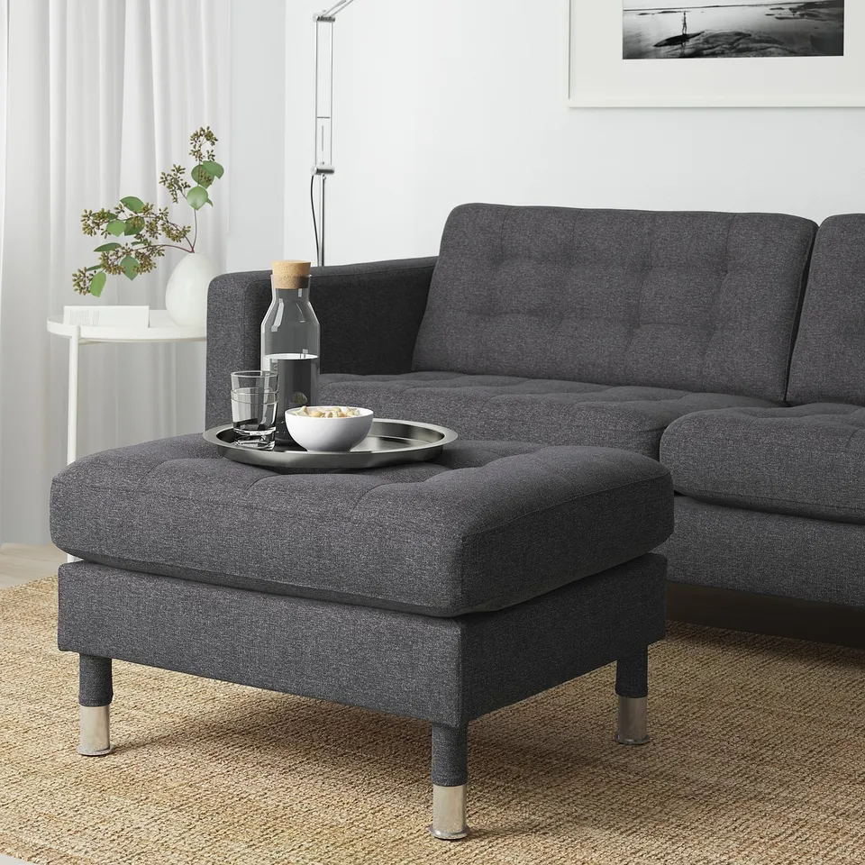 Modern living room with LANDSKRONA footstool, sofa, and vase of dried flowers. Black and white artwork on wall.