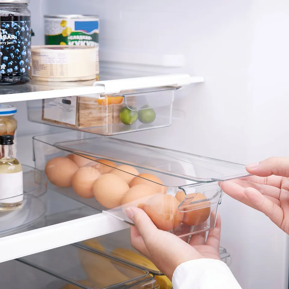 Person taking a plastic egg container from a fridge, showing organised food storage with clear lid for easy visibility.