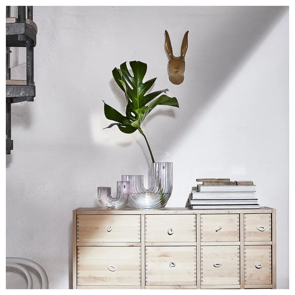 A light wood dresser with a glass rainbow vase holding green plant.