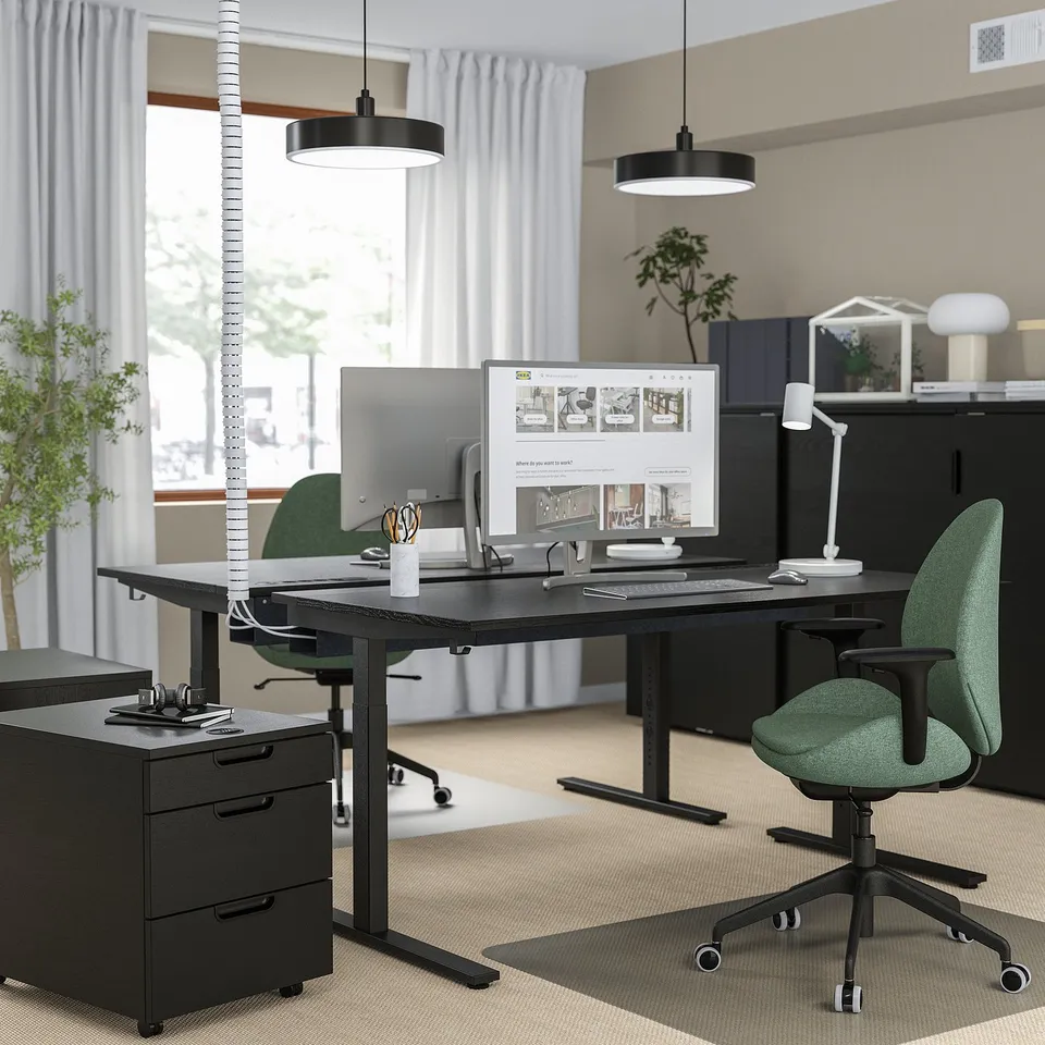 Modern home office with MITTZON black desk, green chairs, large screens, organised with minimalist design.