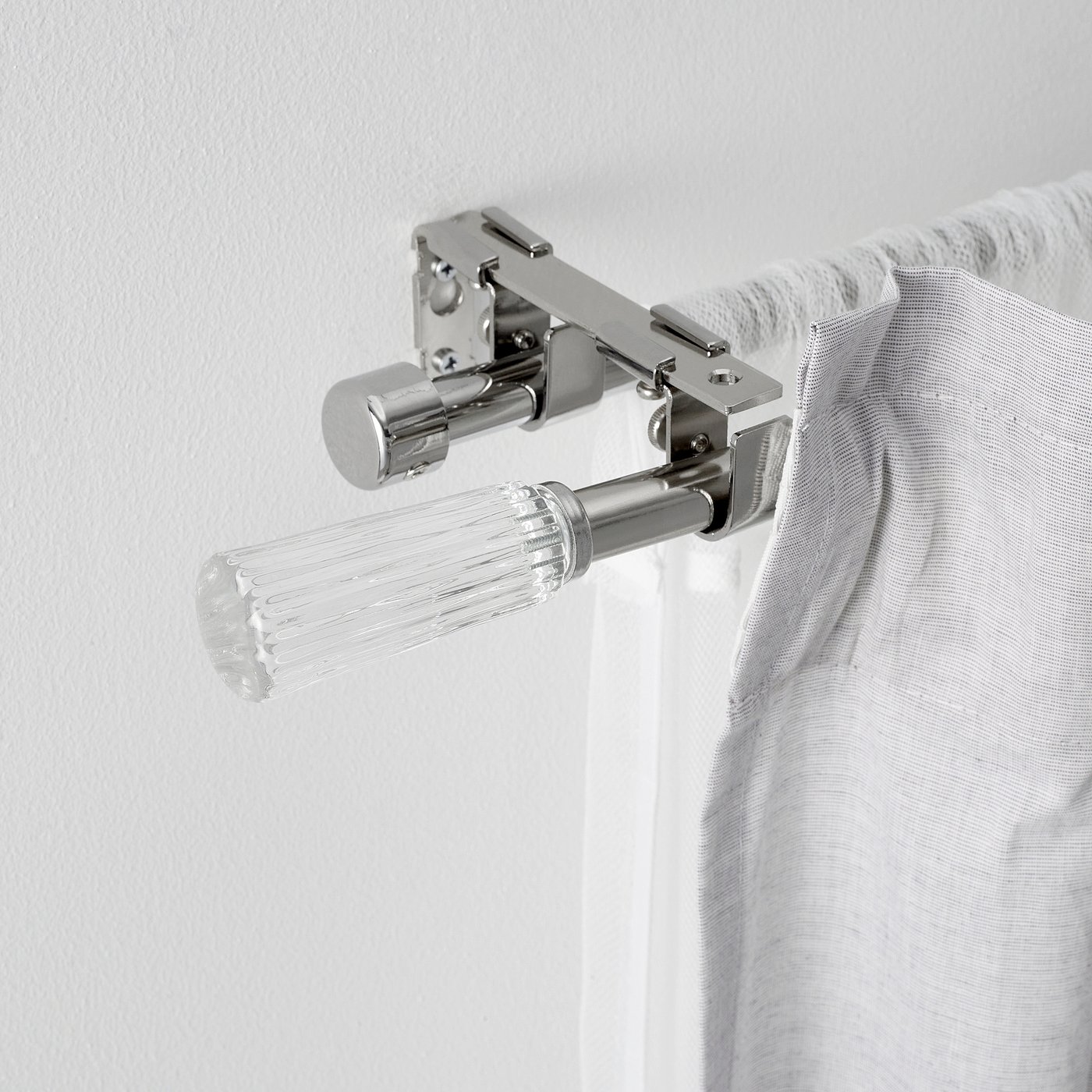 Modern chrome curtain rod with clear glass finials, mounted on wall for elegant window dressing.