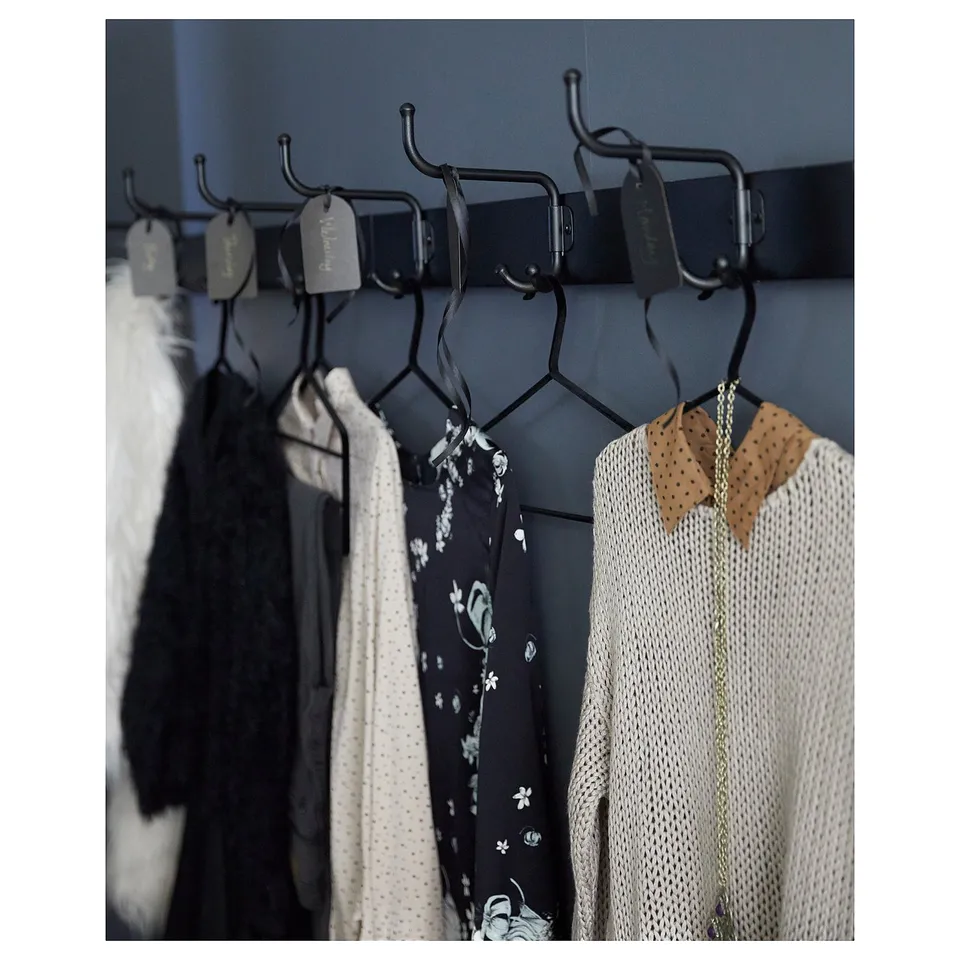 Black metal clothes rack with multiple hooks, holding various garments including a sweater with a bowtie and a floral dress.