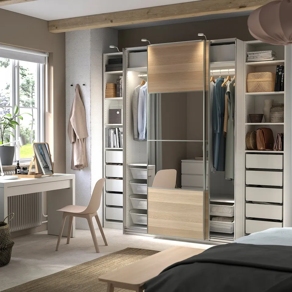 A modern bedroom a light wood and grey PAX wardrobe system, with sliding doors and built-in shelves holding clothes and decorative items.