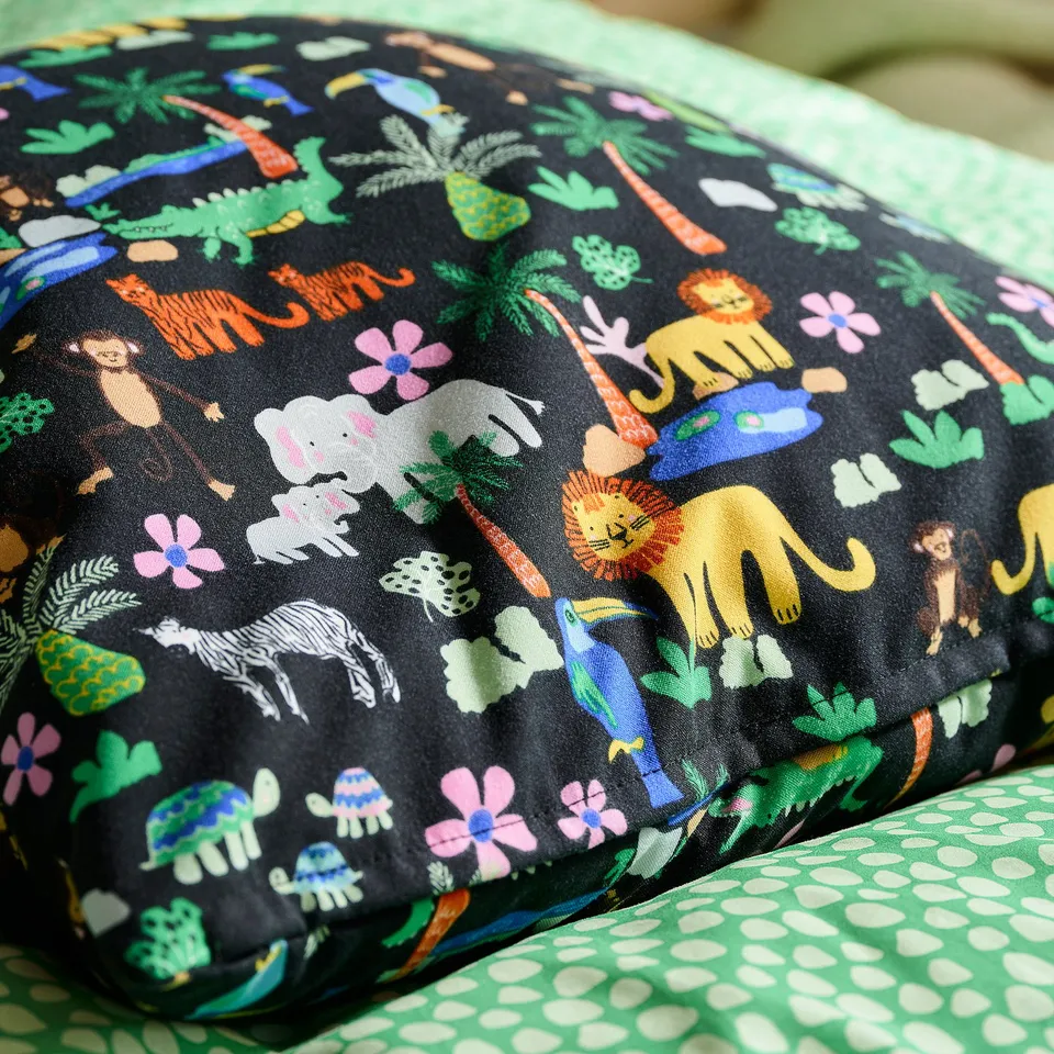 Jungle-themed pillow with vibrant, colourful animals on black fabric, resting on a green patterned surface.